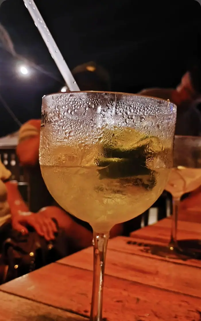 Gin tônica gelada numa taça alta, com limão e gelo, na mesa de madeira